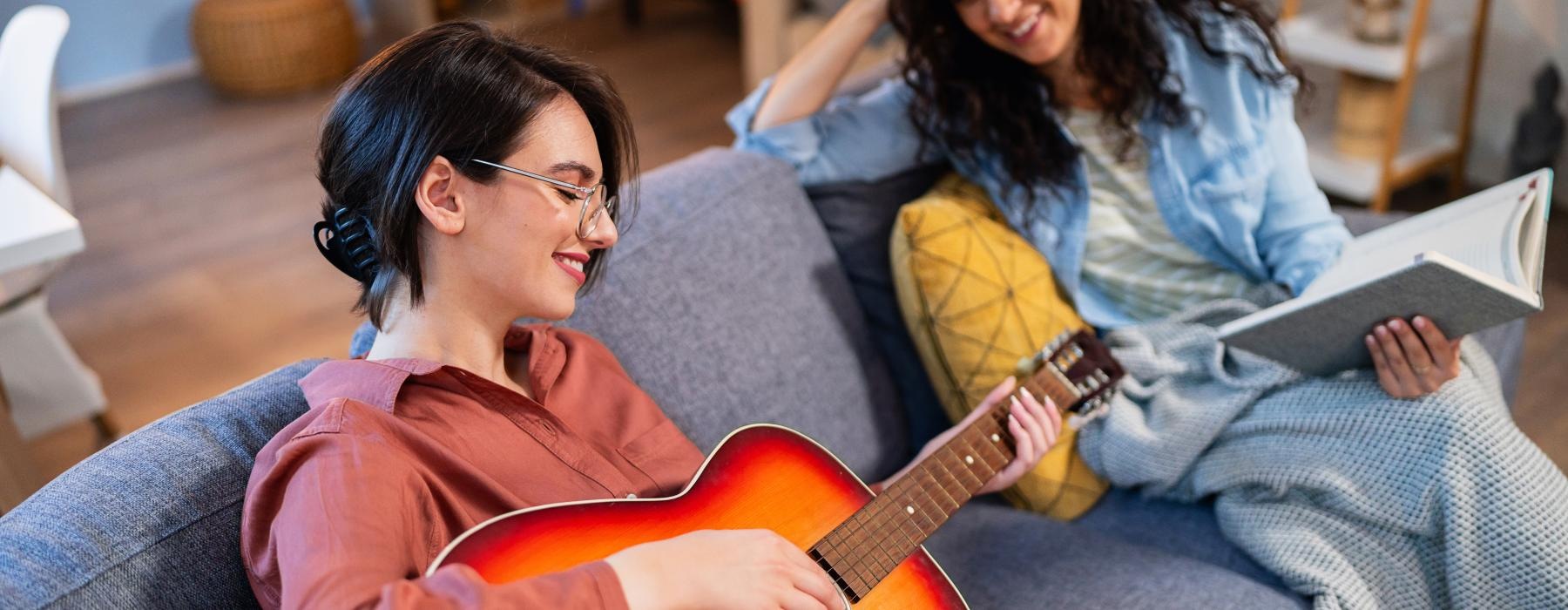 a person playing a guitar next to a person sitting on a couch