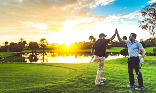 two men high-fiving while playing golf in front of a sunset