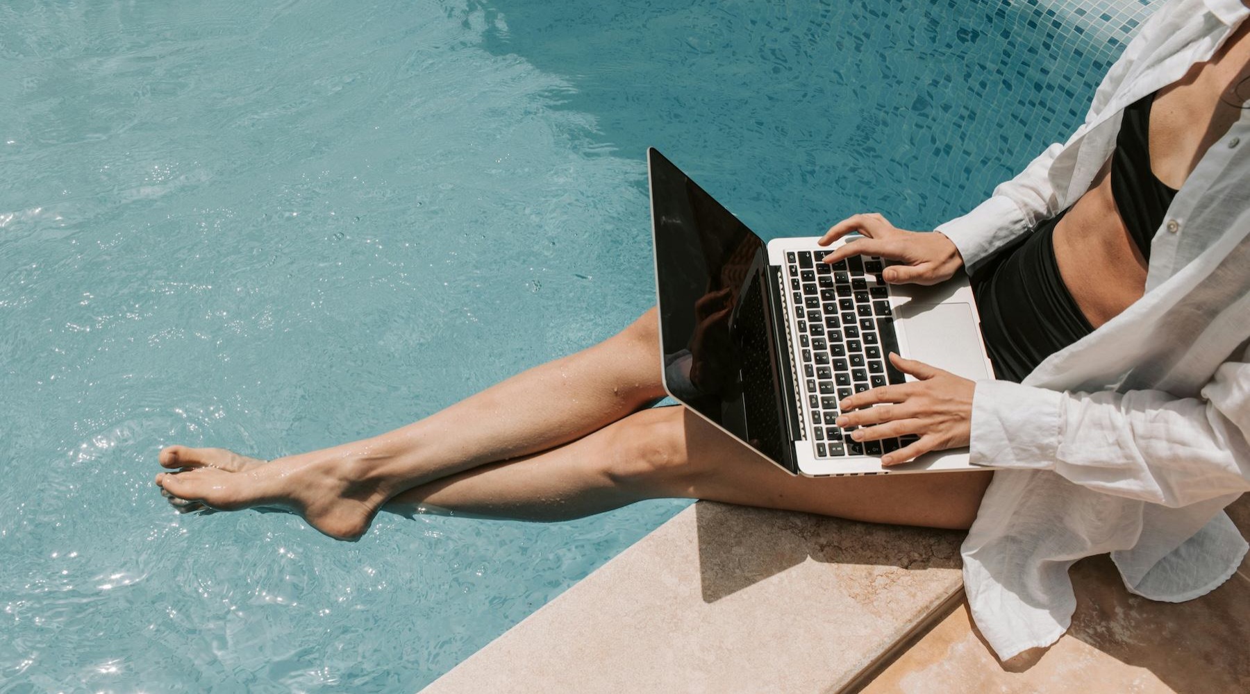 a person sitting by a pool working on a laptop
