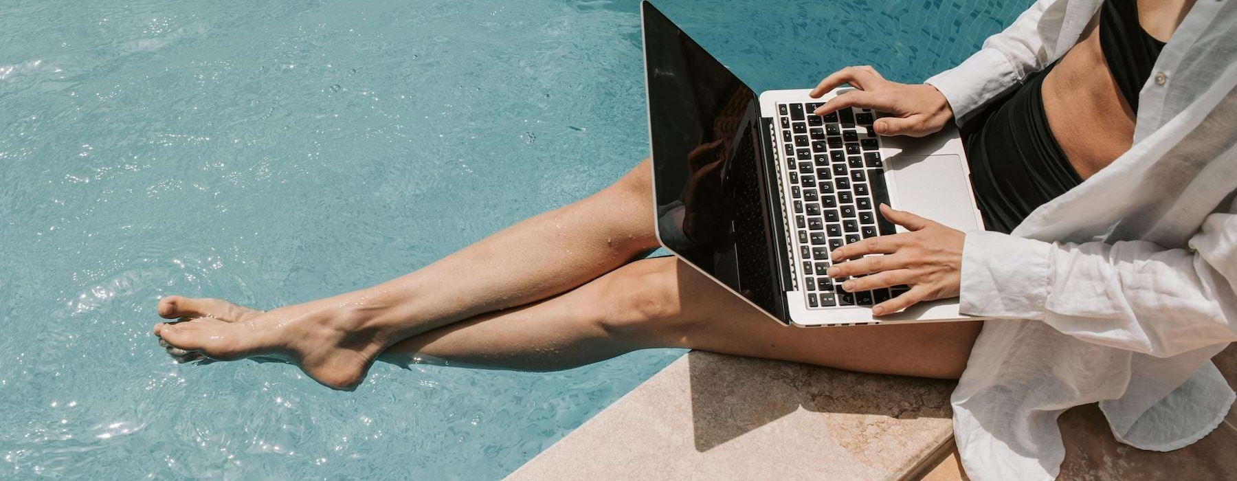a person sitting by a pool working on a laptop