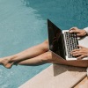 a person sitting by a pool working on a laptop